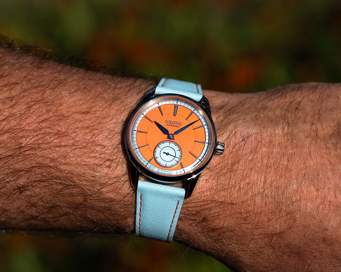 GRØNE Horologium Something Quirky orange dial on a light-blue strap worn on wrist.